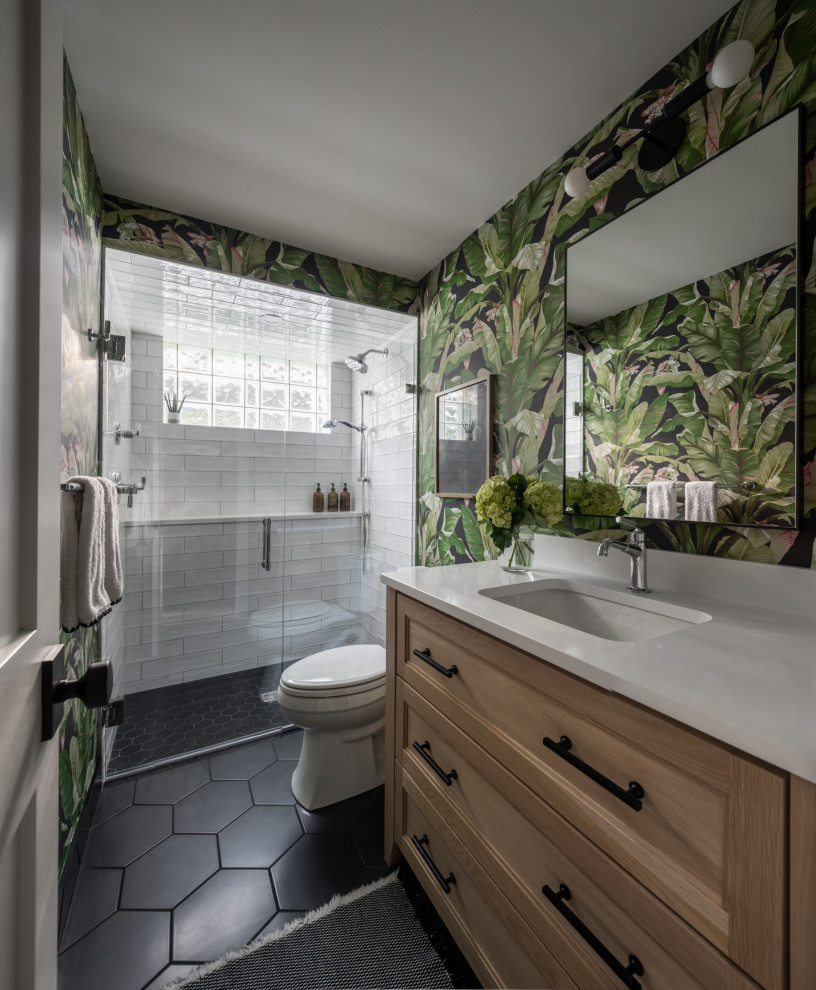 This is an example of a medium sized coastal bathroom in Minneapolis with shaker cabinets, light wood cabinets, an alcove shower, a two-piece toilet, white tiles, metro tiles, green walls, porcelain flooring, a submerged sink, engineered stone worktops, black floors, a hinged door, white worktops, a wall niche, a single sink, a freestanding vanity unit and wallpapered walls.