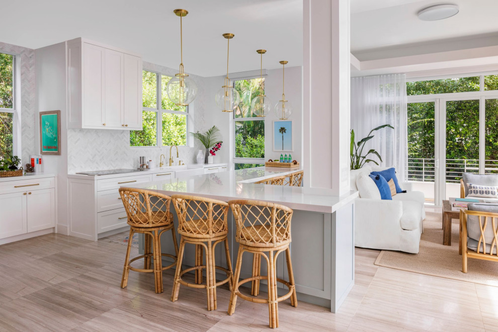 Photo of a mid-sized beach style l-shaped kitchen in Miami with a farmhouse sink, beaded inset cabinets, white cabinets, quartzite benchtops, white splashback, porcelain splashback, panelled appliances, with island, white benchtop, medium hardwood floors and brown floor.