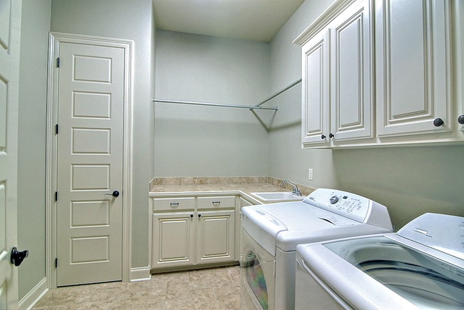 Large traditional l-shaped laundry room in New Orleans with raised-panel cabinets, white cabinets, tile benchtops, white walls, porcelain floors, a side-by-side washer and dryer and a drop-in sink.