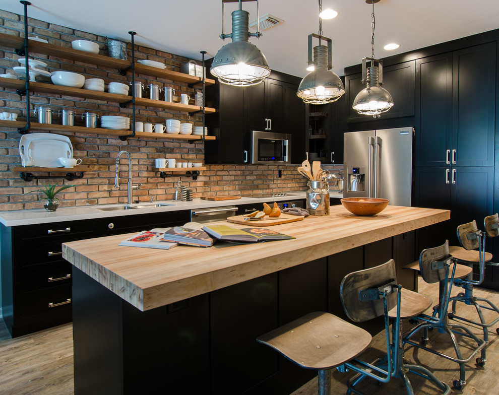 Small industrial l-shaped kitchen in Miami with a double-bowl sink, shaker cabinets, black cabinets, wood benchtops, stainless steel appliances, with island, red splashback, brick splashback, light hardwood floors, brown floor and white benchtop.