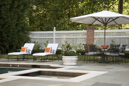 A tall vinyl pool fence surrounding a luxurious backyard patio and pool complex.