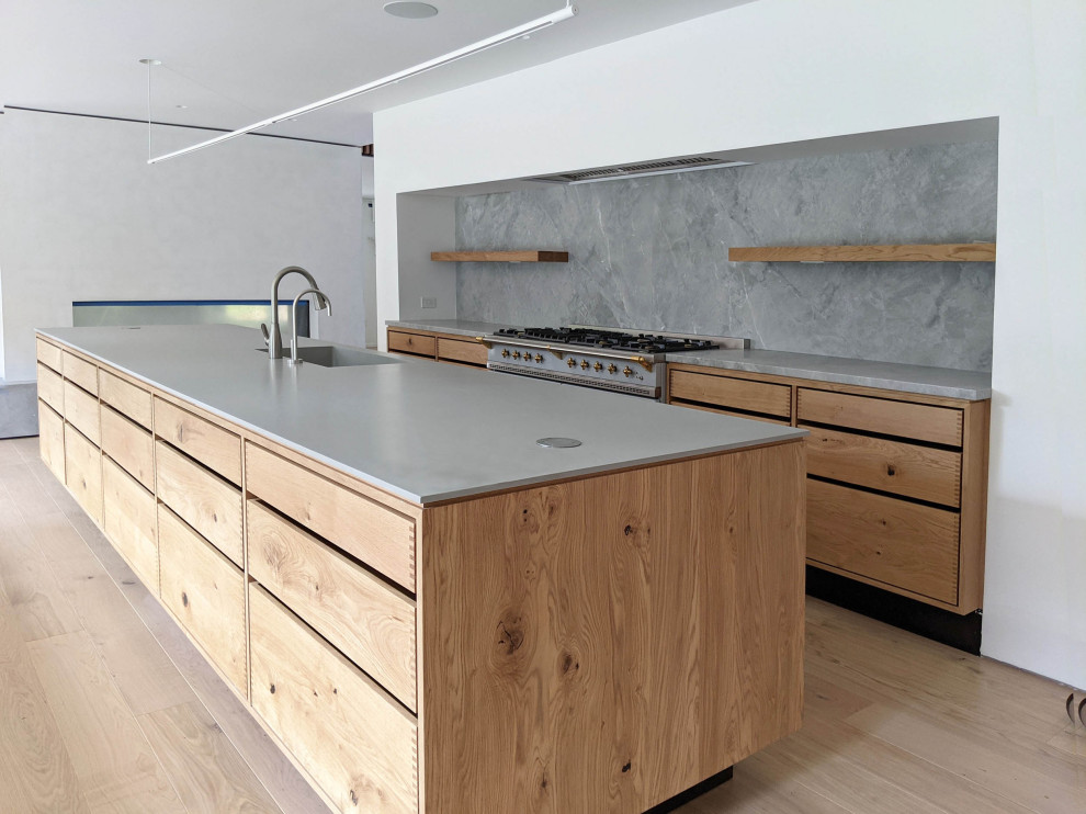 Bild på ett mycket stort nordiskt grå linjärt grått kök med öppen planlösning, med släta luckor, beige skåp, bänkskiva i kvarts, blått stänkskydd, stänkskydd i marmor, rostfria vitvaror och en köksö