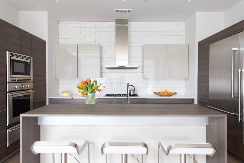 This is an example of a contemporary kitchen in Atlanta with flat-panel cabinets, white cabinets, white splashback, subway tile splashback, stainless steel appliances, with island and white benchtop.