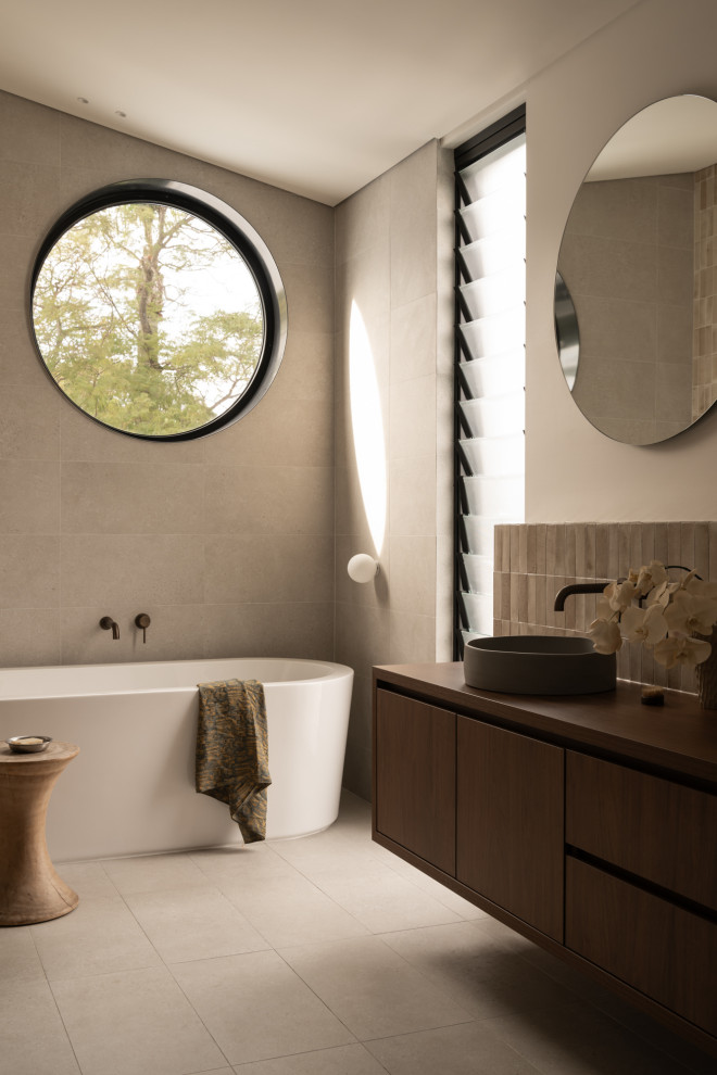 Photo of a midcentury master bathroom in Perth with flat-panel cabinets, dark wood cabinets, a freestanding tub, gray tile, grey walls, a vessel sink, wood benchtops, grey floor, brown benchtops, a floating vanity and vaulted.