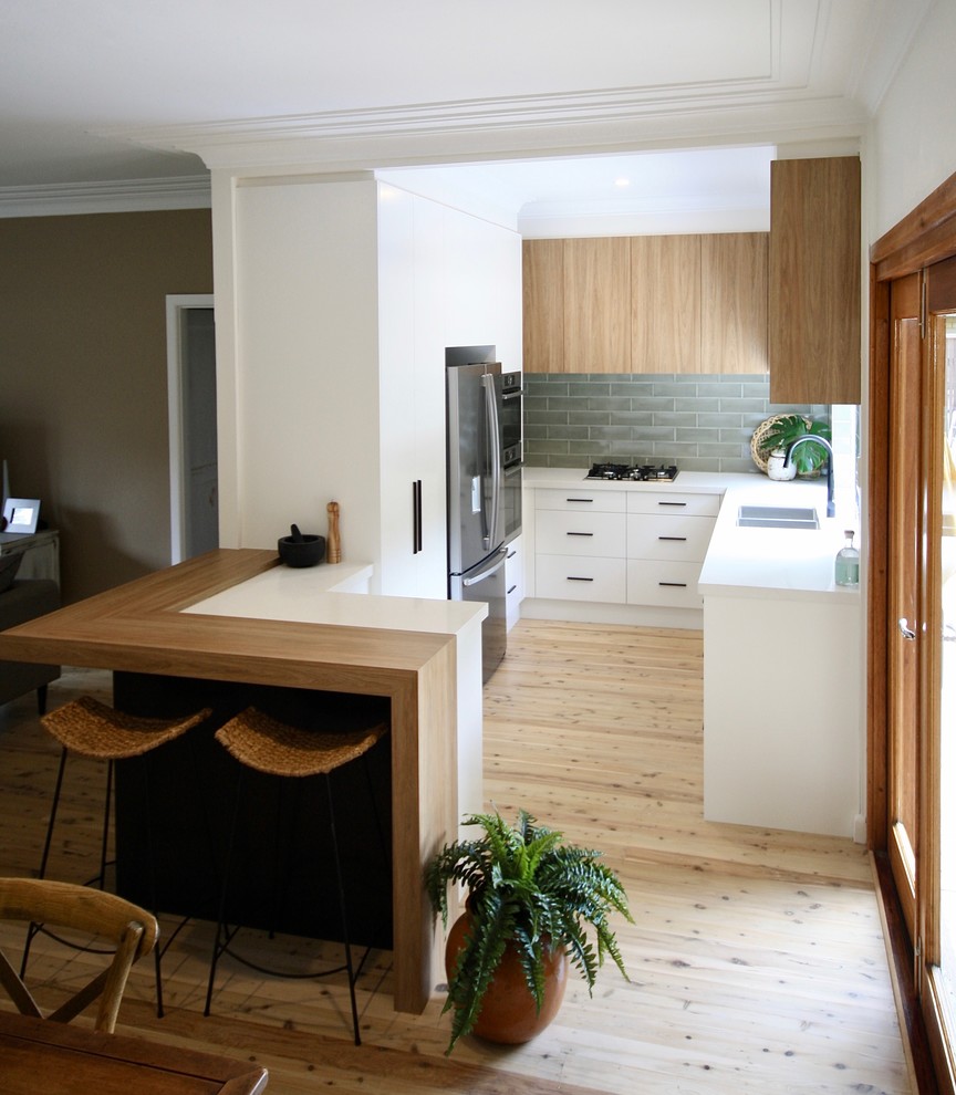 Inspiration for a mid-sized modern u-shaped open plan kitchen in Sydney with an undermount sink, flat-panel cabinets, white cabinets, quartz benchtops, green splashback, subway tile splashback, stainless steel appliances, medium hardwood floors, no island, brown floor and white benchtop.