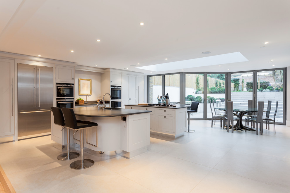 This is an example of an expansive transitional eat-in kitchen in London with an undermount sink, recessed-panel cabinets, white cabinets and stainless steel appliances.