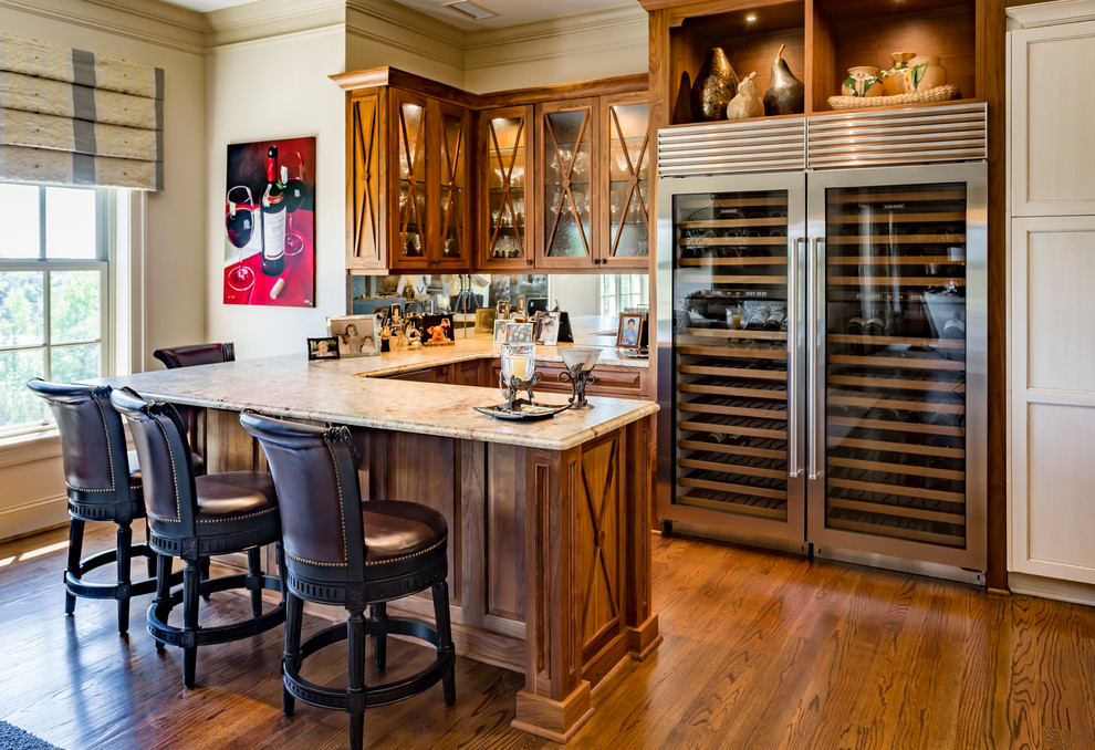 Photo of a mid-sized transitional u-shaped home bar in Charlotte with raised-panel cabinets, medium wood cabinets, granite benchtops, mirror splashback, medium hardwood floors and brown floor.