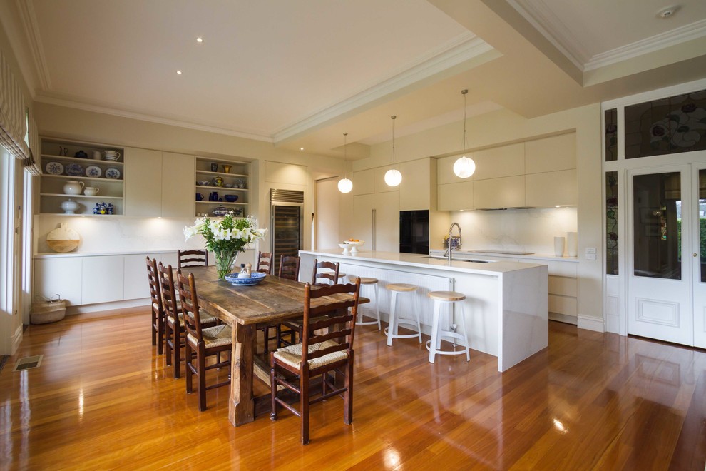 Expansive contemporary l-shaped eat-in kitchen in Melbourne with an undermount sink, flat-panel cabinets, white cabinets, quartz benchtops, stone slab splashback, black appliances, medium hardwood floors and with island.