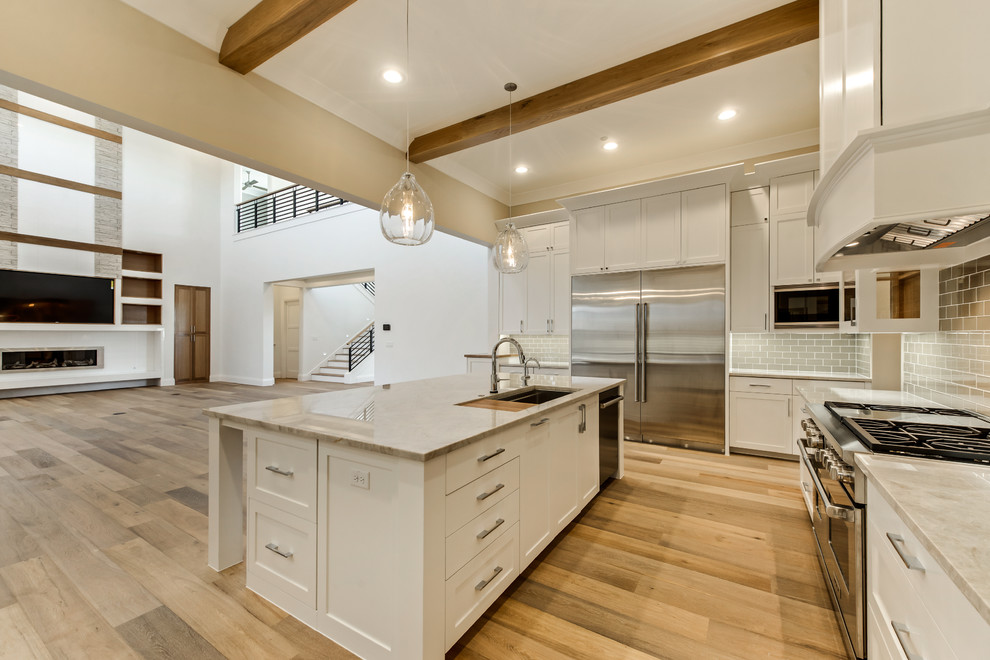 Photo of a large contemporary u-shaped eat-in kitchen in Dallas with an undermount sink, flat-panel cabinets, white cabinets, quartzite benchtops, brown splashback, glass tile splashback, stainless steel appliances, light hardwood floors and with island.