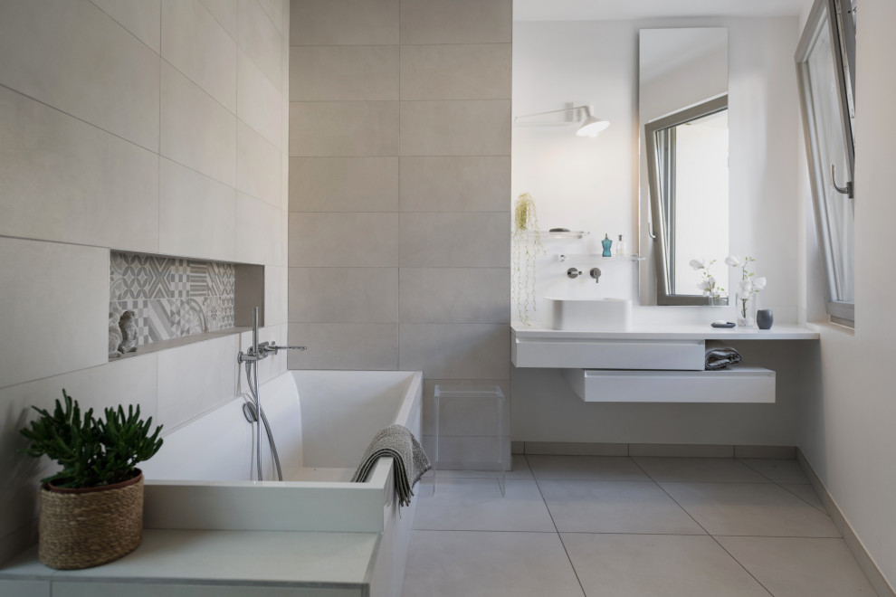 This is an example of a mid-sized contemporary master bathroom in Lyon with white cabinets, an alcove tub, beige tile, porcelain tile, white walls, porcelain floors, a vessel sink, beige floor and white benchtops.