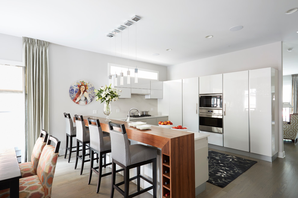 Photo of a contemporary eat-in kitchen in Chicago with flat-panel cabinets, white cabinets, stainless steel appliances, a peninsula and medium hardwood floors.