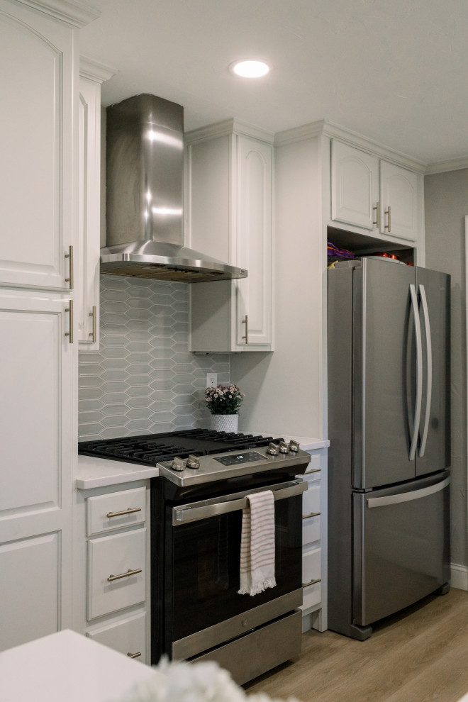 Modern inredning av ett mellanstort vit vitt u-kök, med luckor med profilerade fronter, vita skåp, grått stänkskydd, stänkskydd i keramik, rostfria vitvaror, en halv köksö och brunt golv