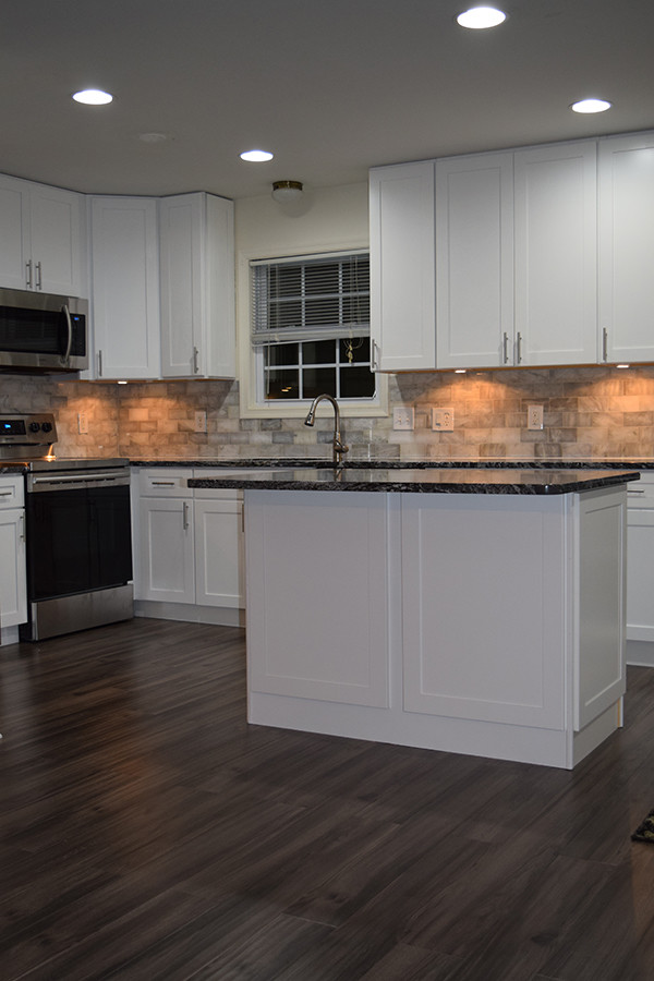 This is an example of a mid-sized transitional l-shaped eat-in kitchen in DC Metro with an undermount sink, shaker cabinets, white cabinets, granite benchtops, white splashback, subway tile splashback, stainless steel appliances, laminate floors, with island and brown floor.