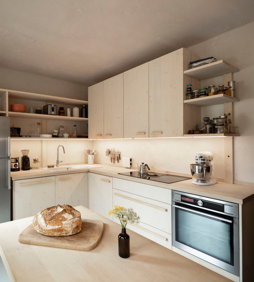 Modern inredning av ett avskilt, litet l-kök, med en nedsänkt diskho, släta luckor, skåp i ljust trä, träbänkskiva, rostfria vitvaror, linoleumgolv och grått golv