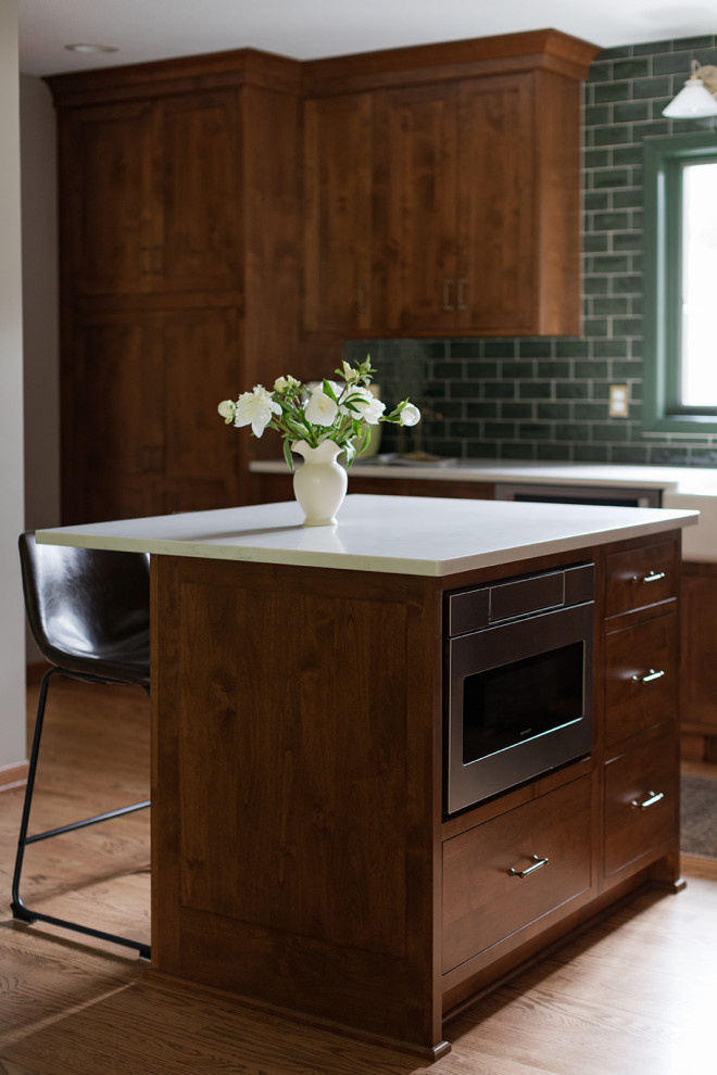 Inspiration for a mid-sized transitional l-shaped medium tone wood floor and brown floor kitchen pantry remodel with a farmhouse sink, shaker cabinets, medium tone wood cabinets, quartz countertops, green backsplash, subway tile backsplash, stainless steel appliances, an island and white countertops