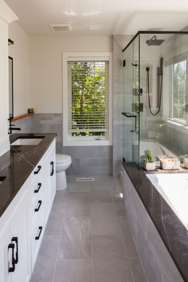 Inspiration for a mid-sized contemporary master bathroom in Calgary with shaker cabinets, white cabinets, an undermount tub, a corner shower, a two-piece toilet, gray tile, porcelain tile, white walls, porcelain floors, an undermount sink, marble benchtops, grey floor, a hinged shower door and black benchtops.