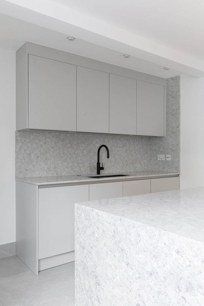 Large contemporary grey and white u-shaped enclosed kitchen in London with an integrated sink, flat-panel cabinets, grey cabinets, engineered stone countertops, grey splashback, stone slab splashback, integrated appliances, porcelain flooring, an island, grey floors and grey worktops.