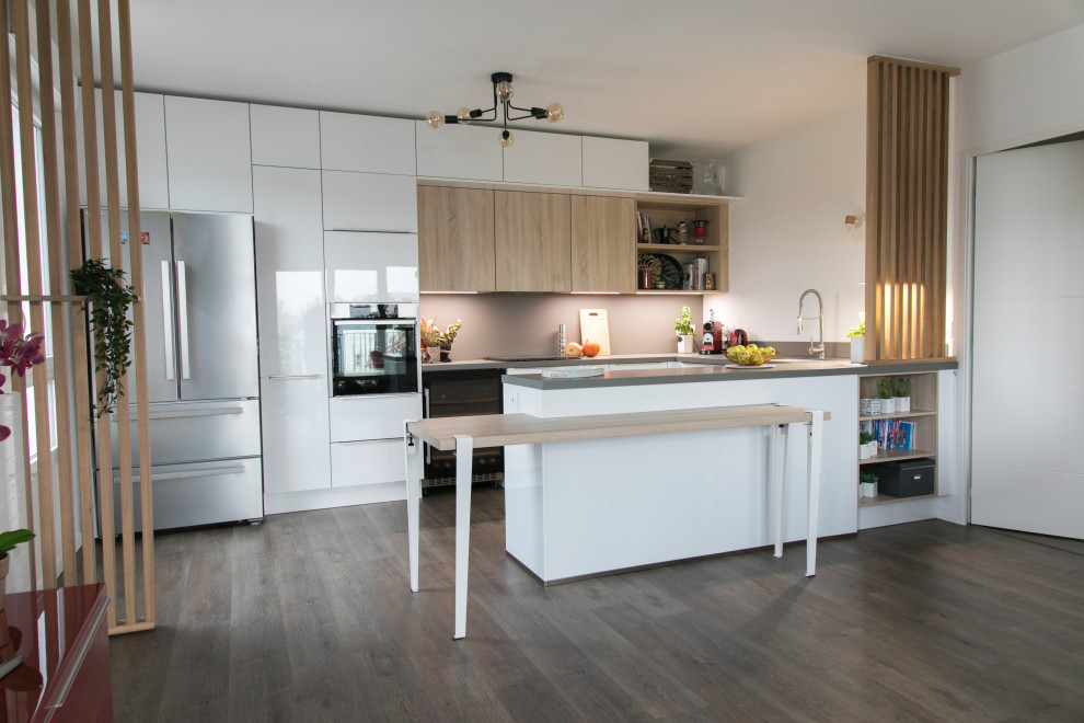 This is an example of a medium sized contemporary u-shaped open plan kitchen in Bordeaux with a submerged sink, flat-panel cabinets, white cabinets, laminate countertops, grey splashback, integrated appliances, medium hardwood flooring, an island and grey worktops.