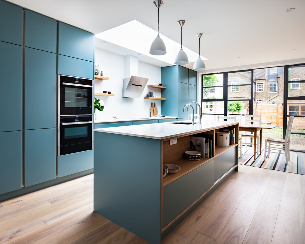 Inspiration for a large contemporary single-wall eat-in kitchen in London with an undermount sink, flat-panel cabinets, blue cabinets, quartzite benchtops, white splashback, glass sheet splashback, black appliances, medium hardwood floors and with island.
