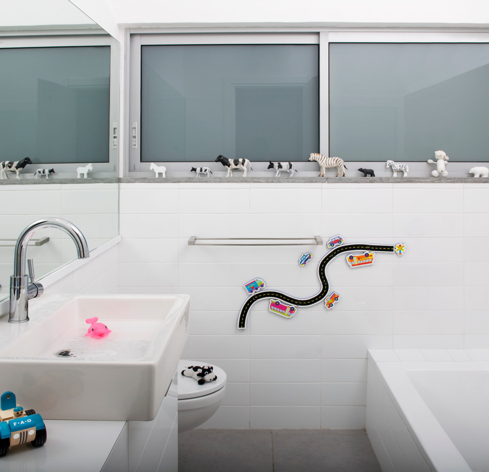 This is an example of a mid-sized contemporary kids bathroom in Other with flat-panel cabinets, white cabinets, wood benchtops, a wall-mount toilet, white tile, ceramic tile, white walls and porcelain floors.