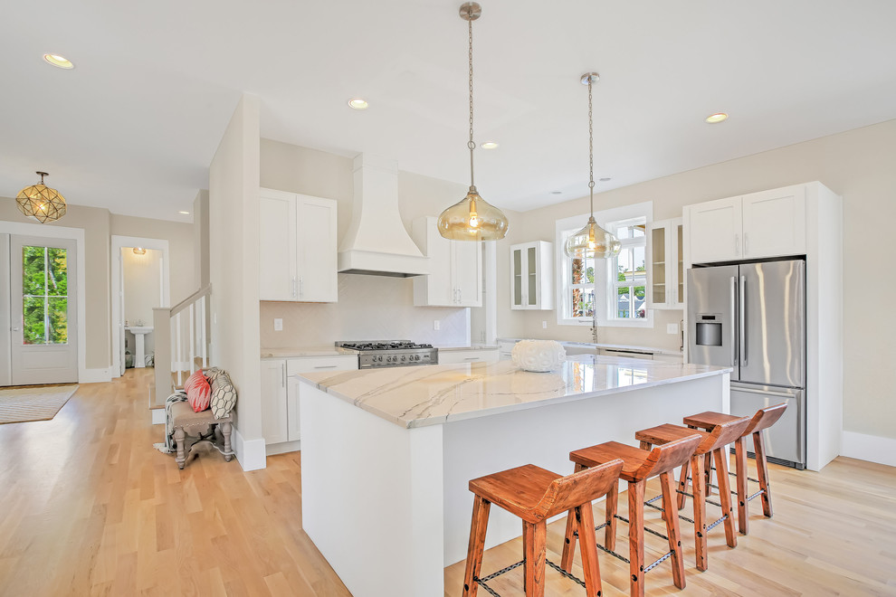 Open concept kitchen - mid-sized transitional l-shaped light wood floor open concept kitchen idea with a farmhouse sink, shaker cabinets, white cabinets, stainless steel appliances, an island, quartzite countertops, white backsplash and ceramic backsplash