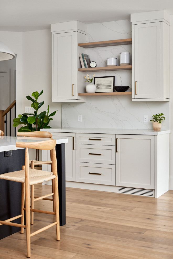 Example of a large transitional single-wall medium tone wood floor and brown floor kitchen pantry design with shaker cabinets, white cabinets, quartz countertops, white backsplash, quartz backsplash, an island and white countertops