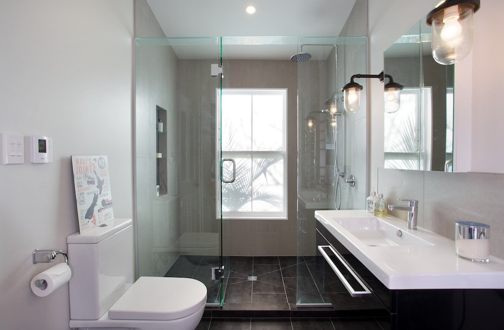 This is an example of a small contemporary master bathroom in Auckland with an integrated sink, flat-panel cabinets, black cabinets, laminate benchtops, a one-piece toilet, gray tile, porcelain tile, grey walls and porcelain floors.
