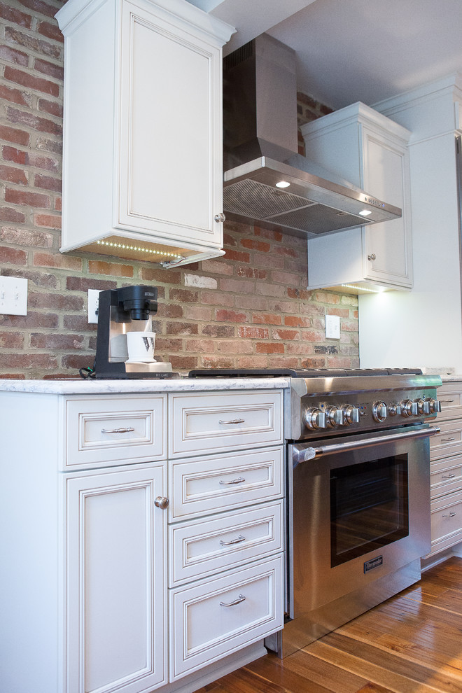 Example of a large transitional medium tone wood floor eat-in kitchen design with an undermount sink, recessed-panel cabinets, black cabinets, quartz countertops, brick backsplash, stainless steel appliances and an island
