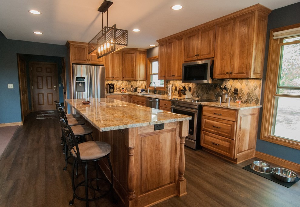 Photo of a mid-sized traditional l-shaped kitchen pantry in Milwaukee with an undermount sink, recessed-panel cabinets, medium wood cabinets, granite benchtops, multi-coloured splashback, terra-cotta splashback, stainless steel appliances, dark hardwood floors, with island and brown floor.