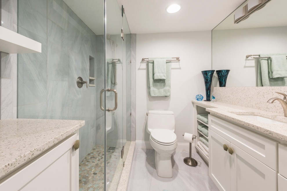 Inspiration for a mid-sized beach style 3/4 bathroom in Orlando with recessed-panel cabinets, white cabinets, a corner shower, gray tile, porcelain tile, grey walls, porcelain floors, an undermount sink, recycled glass benchtops, grey floor, a hinged shower door and white benchtops.