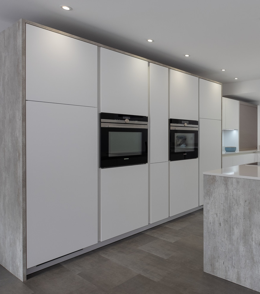 Photo of a mid-sized industrial l-shaped open plan kitchen in Hampshire with an undermount sink, flat-panel cabinets, white cabinets, quartzite benchtops, white splashback, stainless steel appliances, linoleum floors, with island, multi-coloured floor and white benchtop.