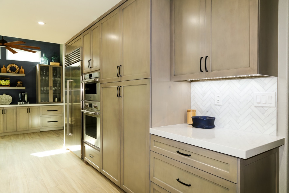 Inspiration for a mid-sized transitional l-shaped separate kitchen in Orange County with shaker cabinets, beige cabinets, quartz benchtops, white splashback, marble splashback, stainless steel appliances, light hardwood floors, with island, brown floor and white benchtop.