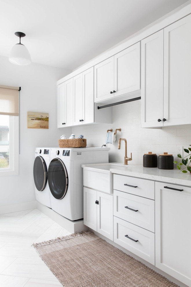 サンフランシスコにある高級な中くらいなビーチスタイルのおしゃれな家事室 (エプロンフロントシンク、白いキャビネット、クオーツストーンカウンター、白いキッチンパネル、サブウェイタイルのキッチンパネル、白い壁、大理石の床、左右配置の洗濯機・乾燥機、マルチカラーの床) の写真
