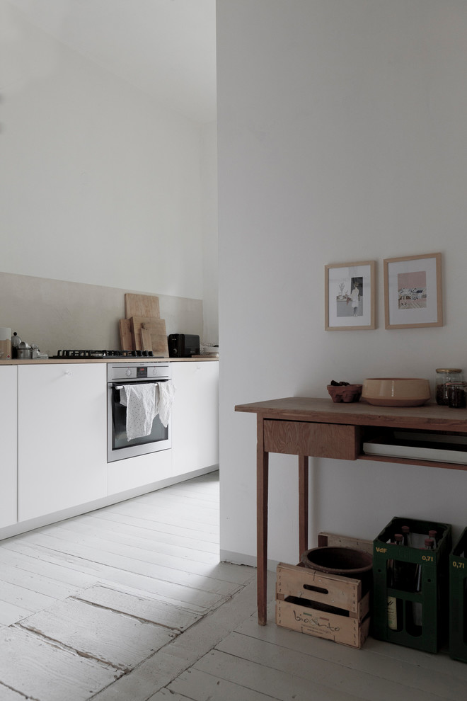 Geschlossene, Zweizeilige, Kleine Skandinavische Küche ohne Insel mit Unterbauwaschbecken, flächenbündigen Schrankfronten, weißen Schränken, Küchenrückwand in Grau, Kalk-Rückwand, Küchengeräten aus Edelstahl, braunem Holzboden und grauem Boden in Leipzig