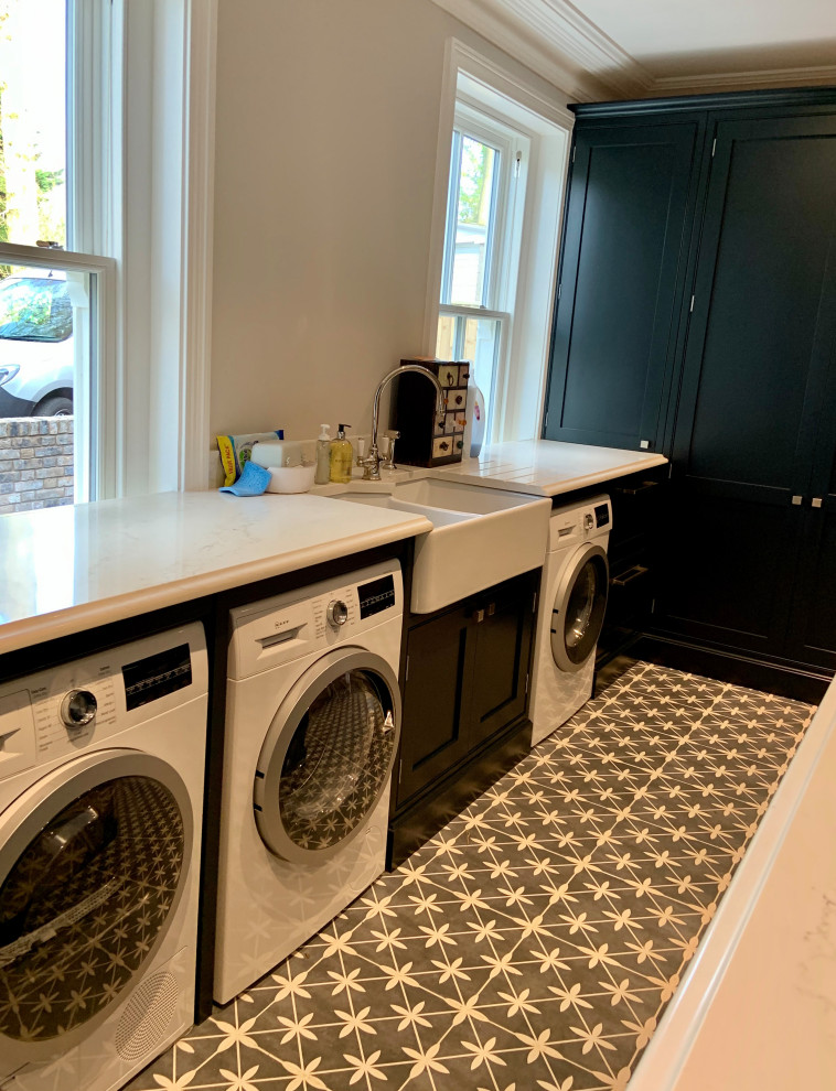 Expansive traditional galley laundry room in Hampshire with an undermount sink, shaker cabinets, black cabinets, quartzite benchtops, white splashback, stone slab splashback, medium hardwood floors, brown floor and white benchtop.