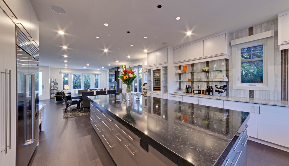 This is an example of a contemporary galley open plan kitchen in Vancouver with flat-panel cabinets, turquoise cabinets, granite benchtops, grey splashback, stone tile splashback and stainless steel appliances.