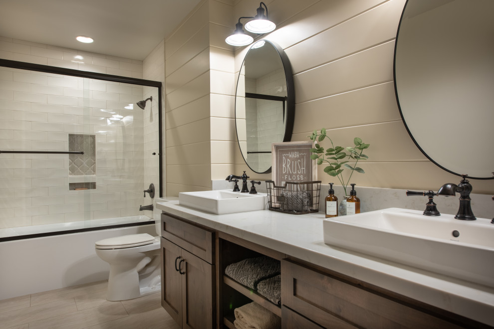 This is an example of a mid-sized country master bathroom in Other with shaker cabinets, brown cabinets, an alcove tub, a shower/bathtub combo, a two-piece toilet, white tile, subway tile, beige walls, ceramic floors, a vessel sink, quartzite benchtops, beige floor, a sliding shower screen and white benchtops.