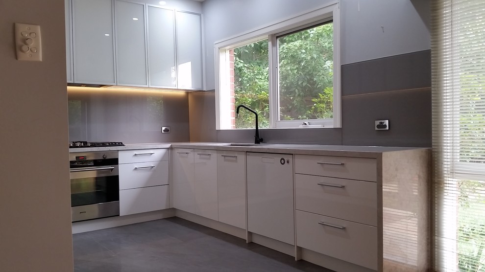 Design ideas for a large contemporary u-shaped kitchen pantry in Melbourne with an undermount sink, yellow cabinets, glass benchtops, grey splashback, glass tile splashback, white appliances, porcelain floors and no island.
