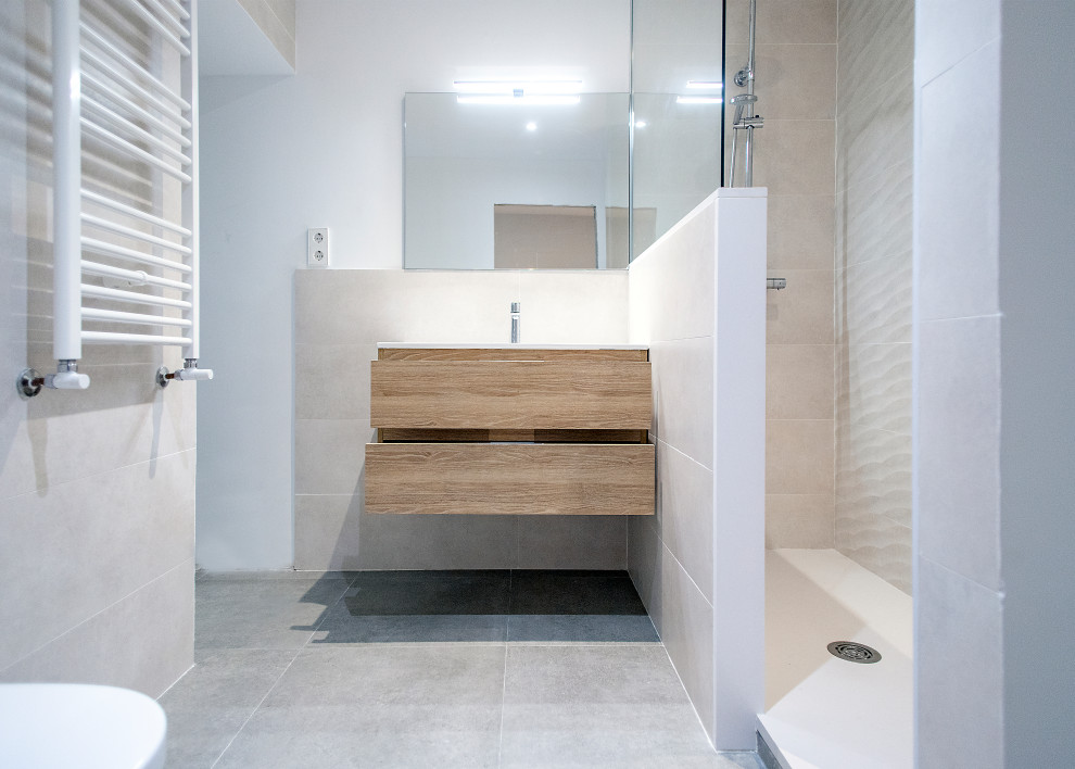 This is an example of a large contemporary master bathroom in Barcelona with flat-panel cabinets, medium wood cabinets, a curbless shower, a one-piece toilet, beige tile, ceramic tile, white walls, ceramic floors, a wall-mount sink, grey floor, an open shower and white benchtops.