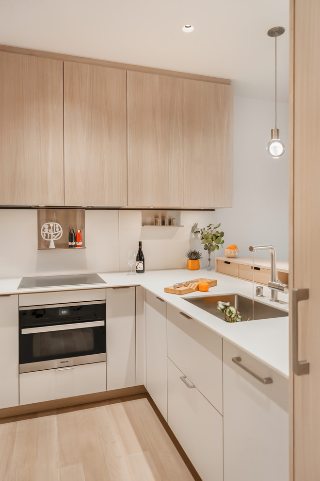 Photo of a small contemporary l-shaped open plan kitchen in Seattle with an undermount sink, flat-panel cabinets, light wood cabinets, quartz benchtops, white splashback, stainless steel appliances, no island and white benchtop.