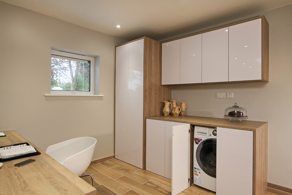 This is an example of an expansive contemporary galley laundry room in Hampshire with flat-panel cabinets, ceramic floors and white cabinets.