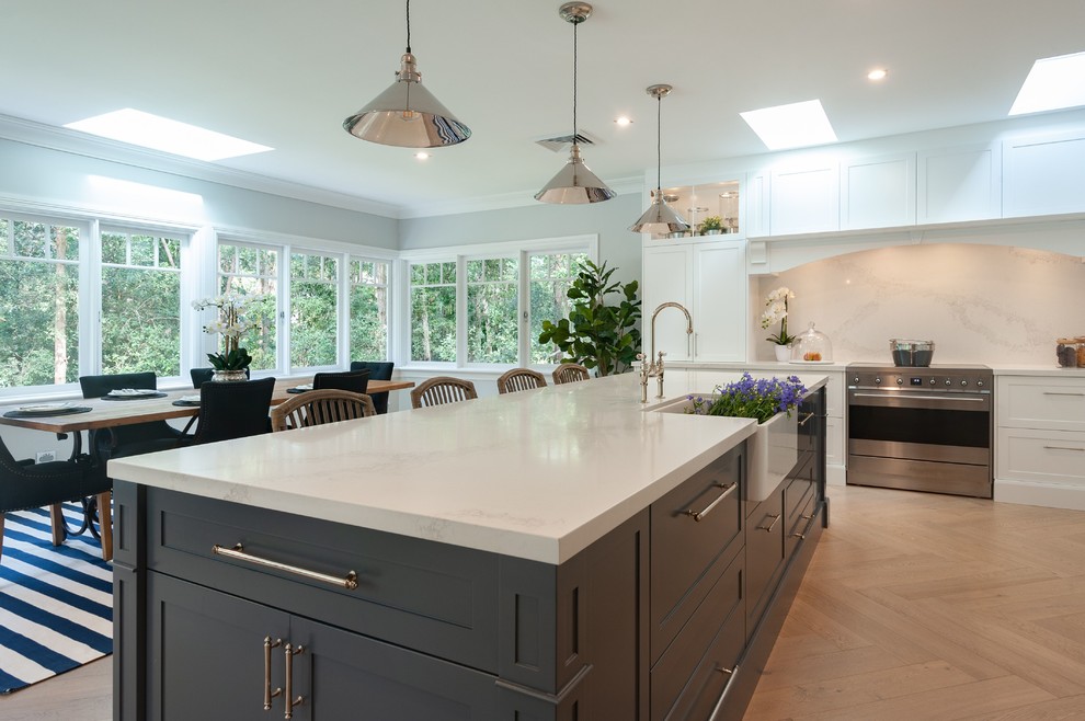 This is an example of an expansive traditional l-shaped eat-in kitchen in Townsville with a farmhouse sink, shaker cabinets, white cabinets, quartz benchtops, white splashback, marble splashback, stainless steel appliances, light hardwood floors, with island and white benchtop.