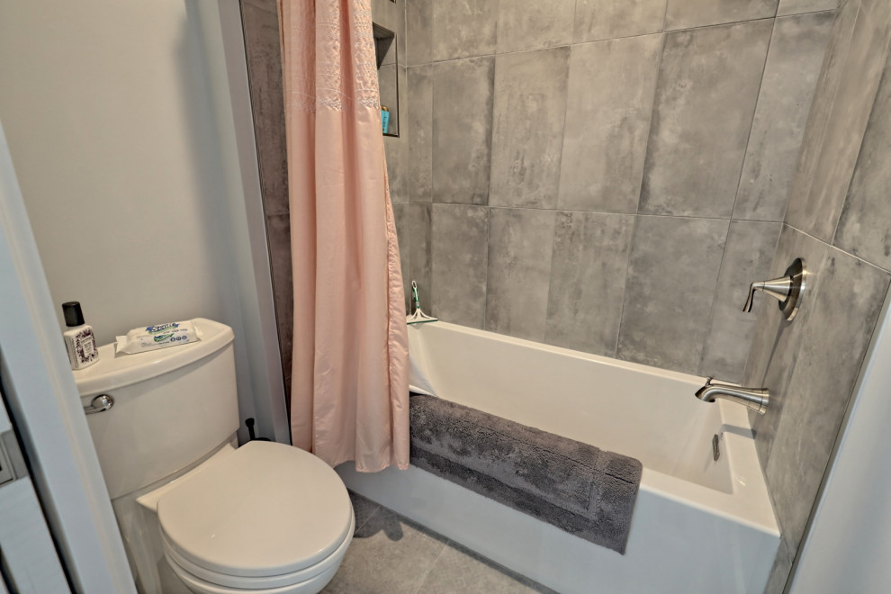 Bild på ett mellanstort vintage flerfärgad flerfärgat badrum, med skåp i shakerstil, vita skåp, ett badkar i en alkov, en dusch/badkar-kombination, en toalettstol med separat cisternkåpa, grå väggar, klinkergolv i keramik, ett undermonterad handfat, granitbänkskiva, grått golv och dusch med duschdraperi