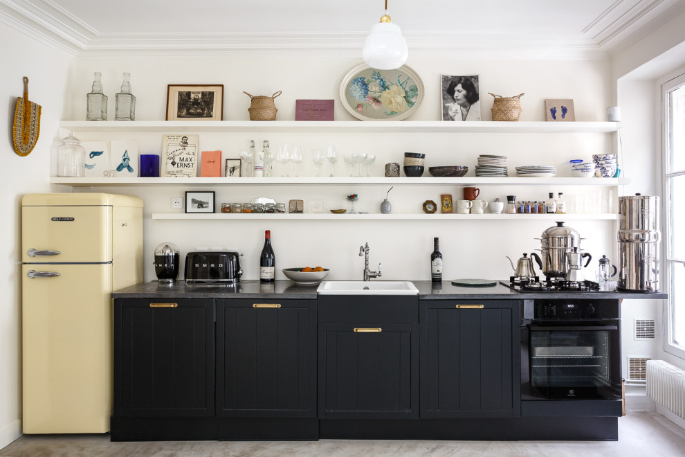 Design ideas for a mid-sized eclectic single-wall separate kitchen in Paris with a farmhouse sink, recessed-panel cabinets, black cabinets, granite benchtops, white splashback, black appliances, ceramic floors, no island, grey floor and black benchtop.