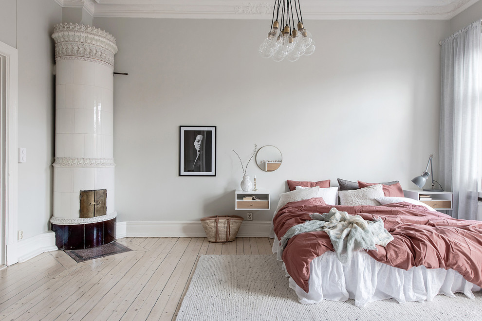 Large scandinavian master bedroom in Gothenburg with grey walls, light hardwood floors, a wood stove, a tile fireplace surround and beige floor.