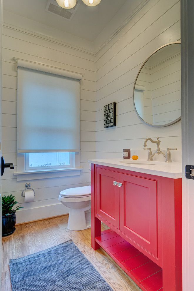 This is an example of a mid-sized country powder room in Other with furniture-like cabinets, white walls, medium hardwood floors, quartzite benchtops, red cabinets, beige floor, an undermount sink and white benchtops.