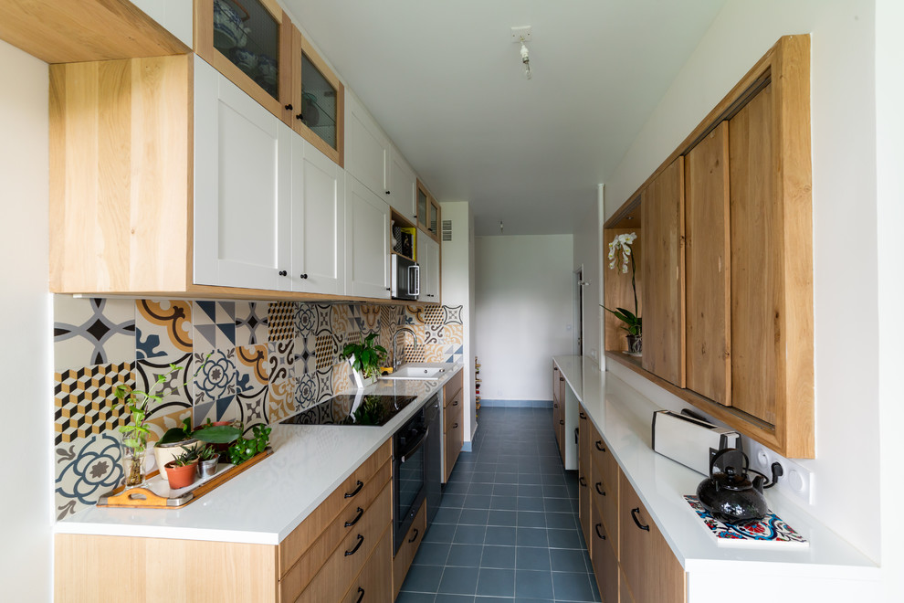 Photo of a mid-sized transitional single-wall kitchen in Paris with laminate benchtops, white benchtop, a drop-in sink, shaker cabinets, light wood cabinets, multi-coloured splashback, mosaic tile splashback, black appliances, no island and black floor.