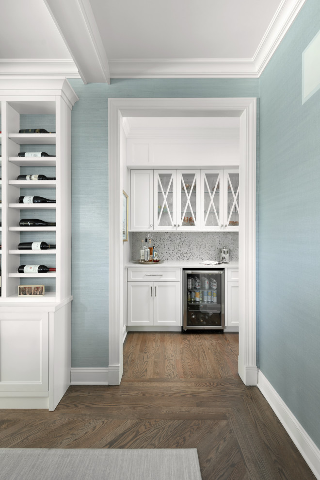 Photo of a large beach style u-shaped kitchen pantry in Chicago with a farmhouse sink, shaker cabinets, white cabinets, quartz benchtops, blue splashback, glass tile splashback, panelled appliances, medium hardwood floors, with island, brown floor and white benchtop.