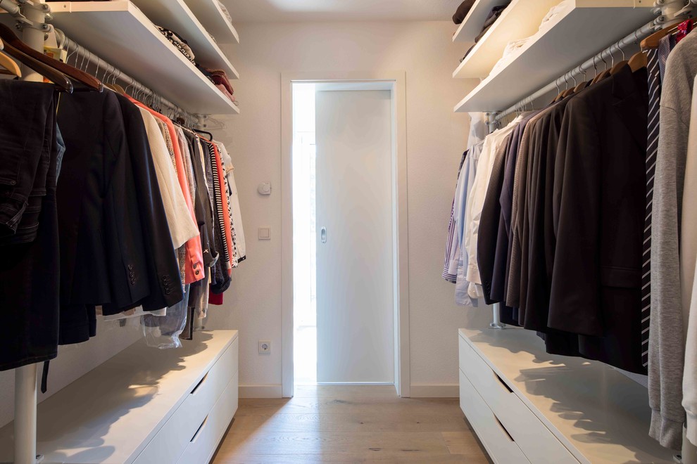 Design ideas for a gender-neutral storage and wardrobe in Other with white cabinets, light hardwood floors and brown floor.