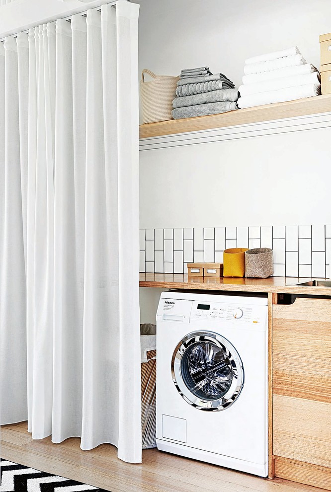 Inspiration for a small scandinavian single-wall utility room in Melbourne with a drop-in sink, flat-panel cabinets, medium wood cabinets, wood benchtops, white walls, painted wood floors, a side-by-side washer and dryer, white floor and beige benchtop.